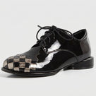 A glossy black patent leather lace-up shoe with a woven metallic silver and black checkerboard pattern on the toe cap, shown against a plain white background.
