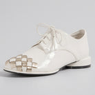 A glossy off-white patent leather lace-up shoe with a woven metallic gold and white patterned toe cap, shown on a plain white background.