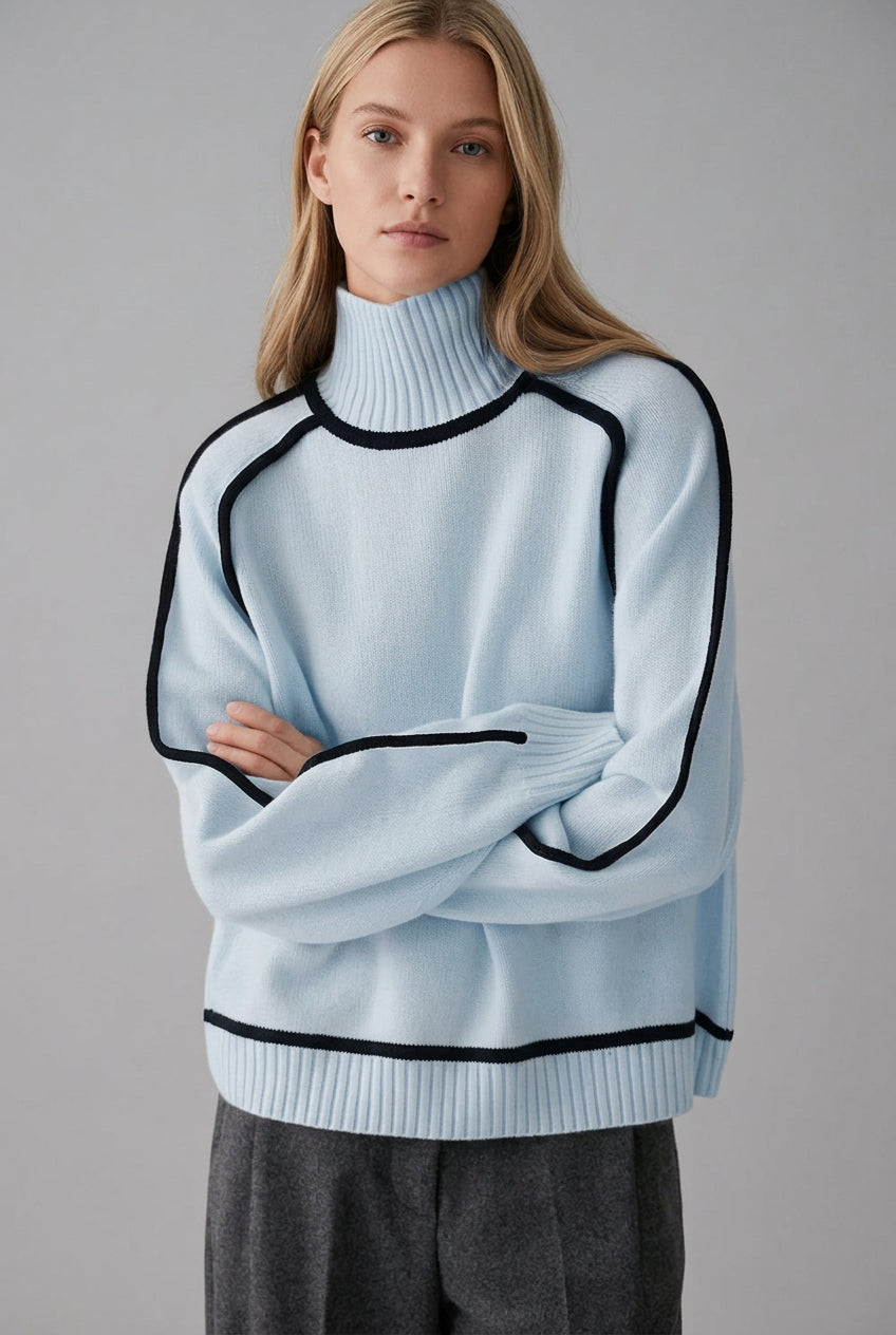 Light blue sweater with black trim worn by a person against a brick wall.